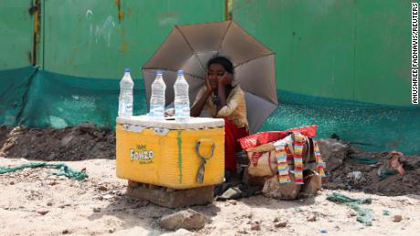 Yeni Delhi'de su satan bir kız güneş ışınlarından korunmak için şemsiye kullanıyor.