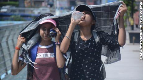 Kızlar, Mumbai'nin kavurucu öğleden sonra sıcağında yürürken ve su içerken başlarını örtüyorlar.