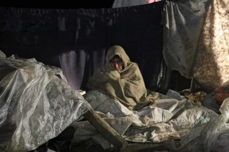 Paktika eyaletinde deprem nedeniyle evsiz kalan bir kadın ısınmaya çalışıyor.