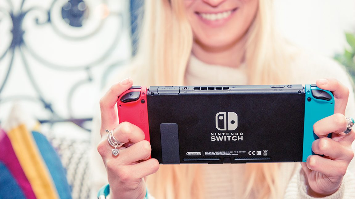Nintendo Switch oyun konsolu oynayan genç bir kadının resmi